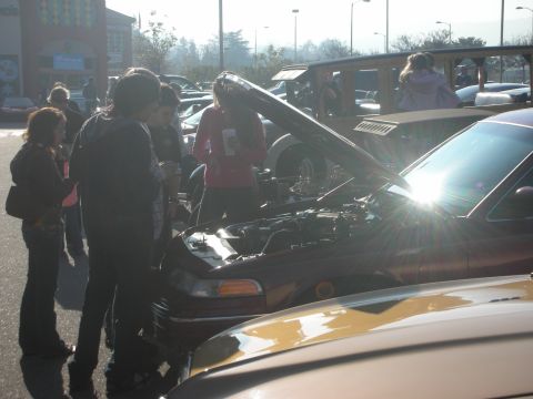 1998 Ford Crown Victoria - A group of people inspect the engine of a maroon 1998 Ford Crown Victoria at a car meet.