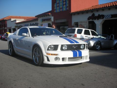 1998 Ford Crown Victoria - A white Ford Mustang with blue racing stripes is parked on a street in front of a building.