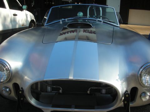 1998 Ford Crown Victoria - A silver Shelby Cobra replica is parked next to a white SUV, showing its distinctive front grille and hood scoop.
