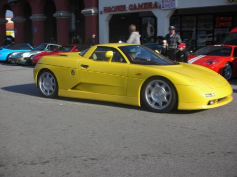 1998 Ford Crown Victoria - A bright yellow sports car is the focus of this scene, with other vehicles visible in the background and a storefront behind them.
