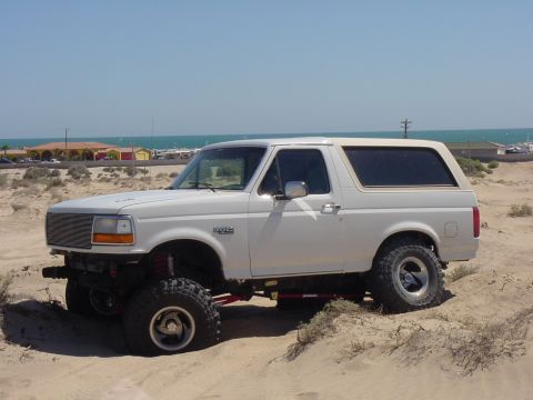 1992 Ford Bronco - This lifted 1992 Ford Bronco is parked on a sandy terrain near the coast.