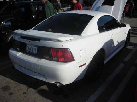 1998 Ford Crown Victoria - A white Ford Mustang is parked in a lot with its hood open, showing off its rear end.