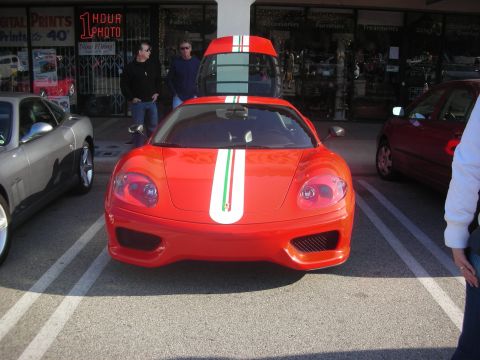 1998 Ford Crown Victoria - A red Ferrari with racing stripes is parked in a lot next to other vehicles, with people standing nearby.