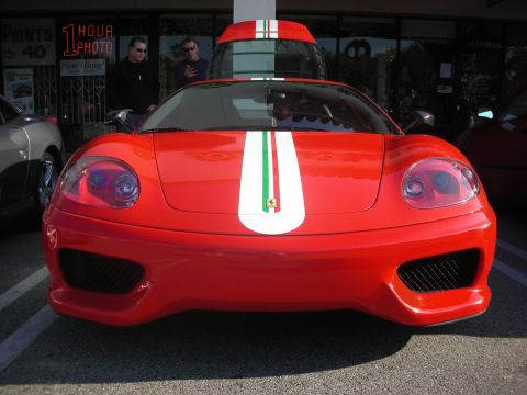 1998 Ford Crown Victoria - A red Ferrari sports car with racing stripes is parked in front of a store with a '1 Hour Photo' sign.