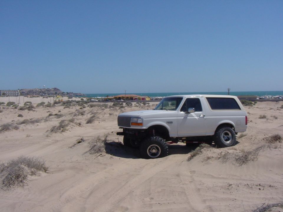 White Ford Bronco parked on sand dunes near the ocean