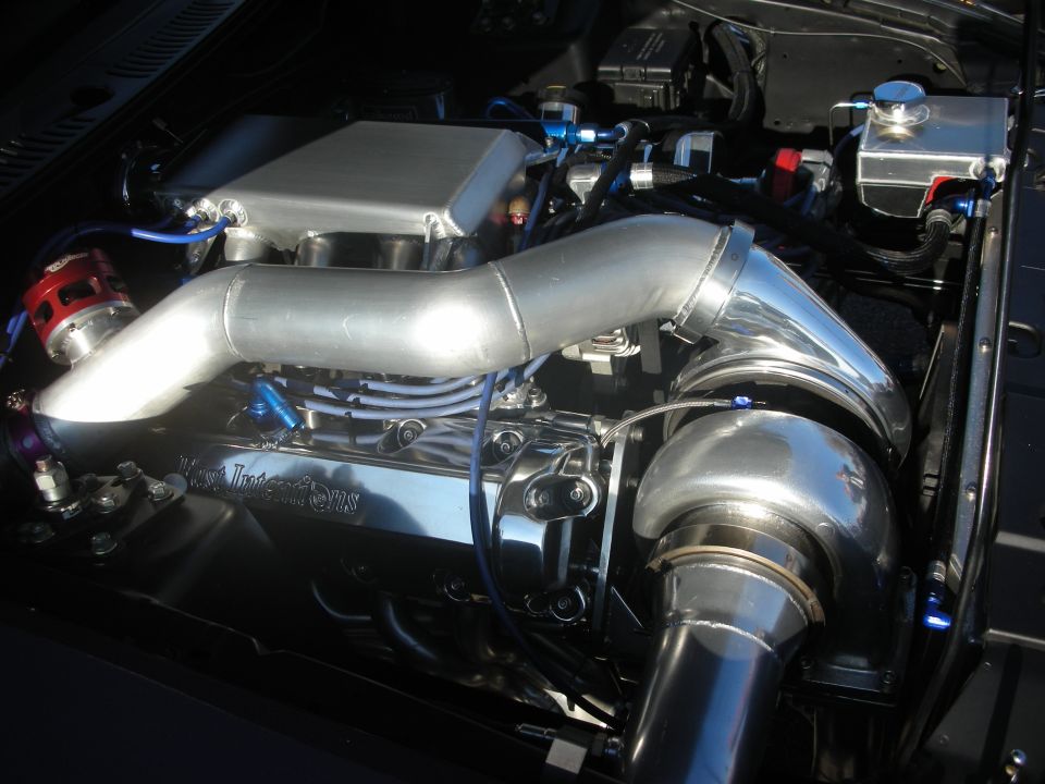 Polished aluminum supercharged engine in an open engine bay with blue and red fittings