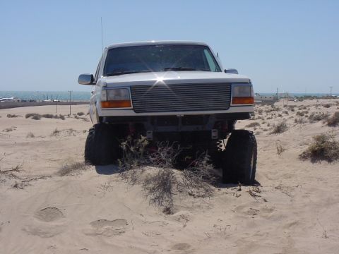 1992 Ford Bronco - This lifted 1992 Ford Bronco is shown on a sandy terrain under a clear blue sky.