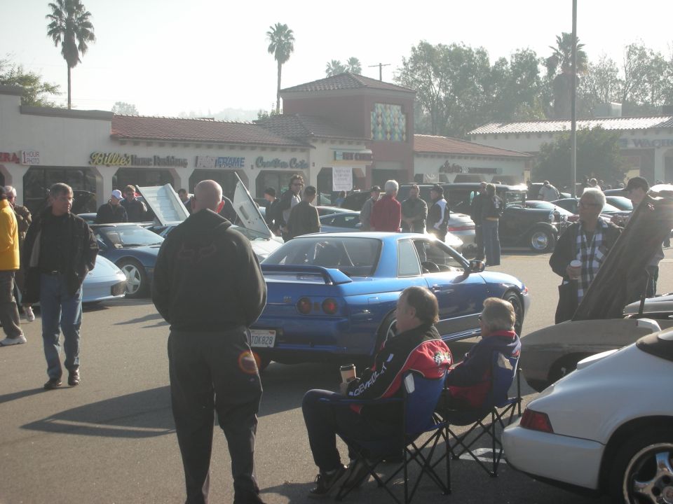 Blue sports coupe among classic cars and people at a sunny outdoor car meet