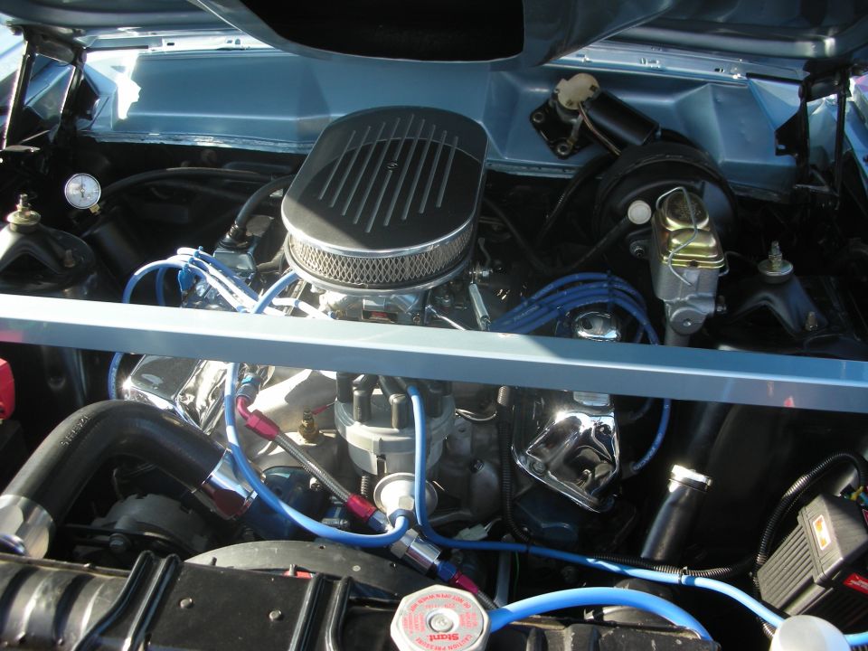 Chromed V8 engine with finned air cleaner and blue plug wires in an open engine bay