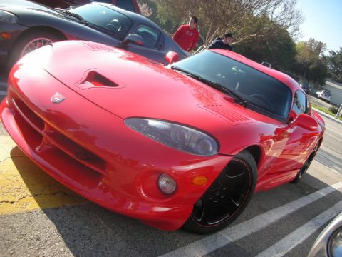 1998 Ford Crown Victoria - A bright red Dodge Viper is parked in a lot, with another car behind it and two people standing nearby.