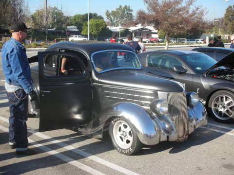 1998 Ford Crown Victoria - A classic black hot rod sedan with chrome accents and racing tires is parked next to a modern car at a meet.