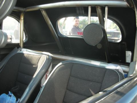 1998 Ford Crown Victoria - The interior of a modified car shows racing seats and a roll cage, with a person seen through the back window.