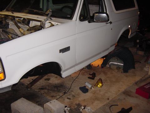 1992 Ford Bronco - The front quarter panel of a white 1992 Ford Bronco is shown with the engine compartment exposed and the vehicle raised on stands.
