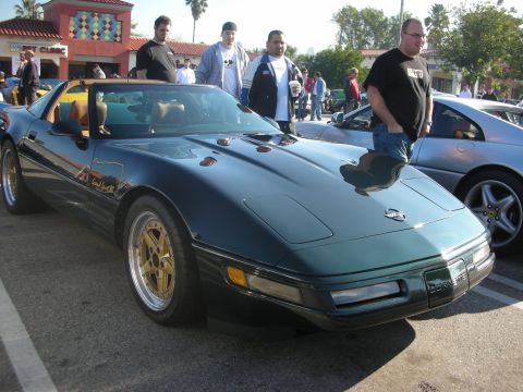 1998 Ford Crown Victoria - A dark green 1996 Chevrolet Corvette C4 Grand Sport convertible is parked at a car meet, gold multi-spoke wheels.