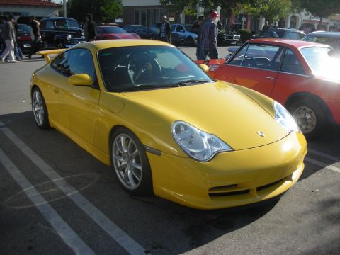 1998 Ford Crown Victoria - A yellow Porsche 911 is parked in a lot with other vehicles and people around.