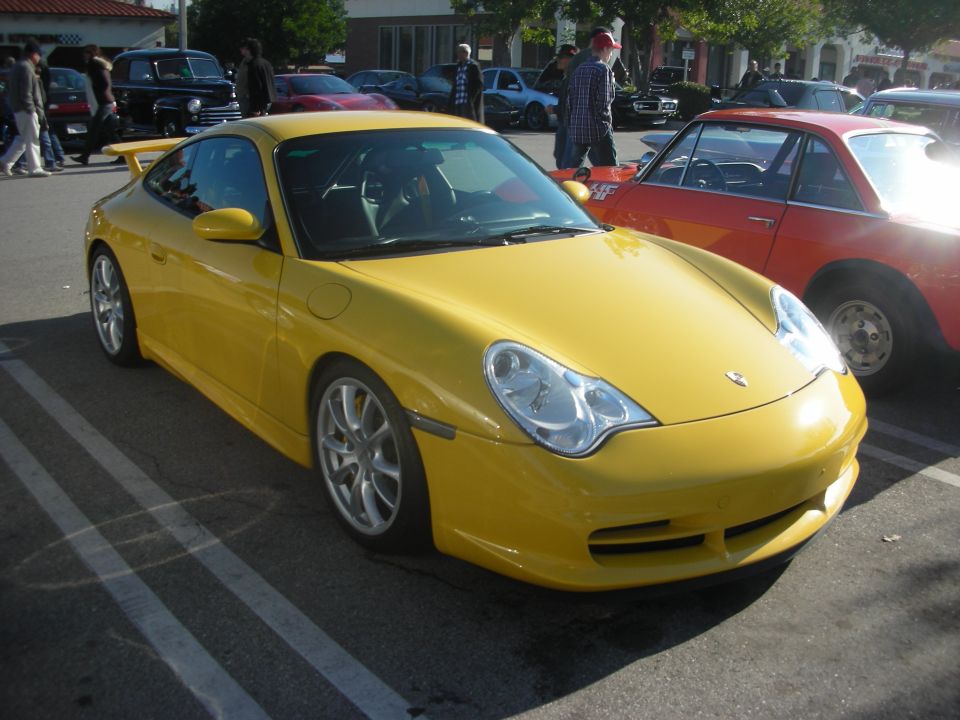 Yellow Porsche 911 GT3 with rear wing parked at a car show