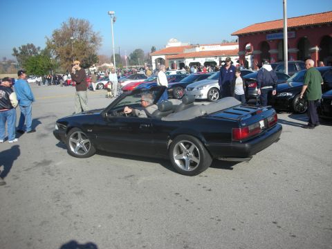 1998 Ford Crown Victoria - A black convertible is parked at an outdoor car meet with other vehicles and people around.