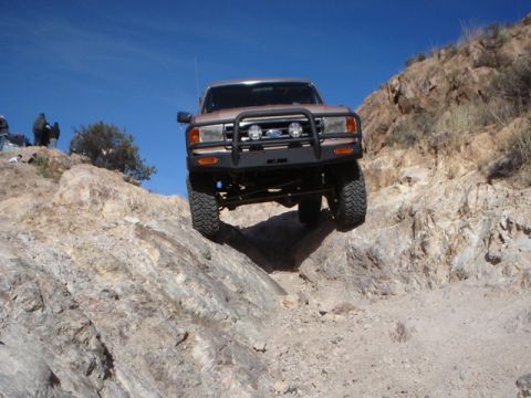 1989 Ford Bronco - A 1987 Ford Bronco navigates a steep, rocky terrain under a clear blue sky.