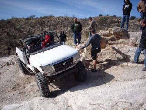 1989 Ford Bronco - Off-road vehicle navigating a steep, rocky incline with spectators present.