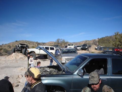 1989 Ford Bronco - Several off-road vehicles are gathered in a desert landscape under a clear blue sky.