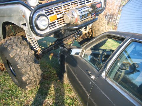 1992 Ford Mustang - An off-road Ford Bronco appears to be resting on top of a sedan, with its large tire positioned on the car's roof.