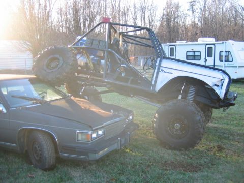 1992 Ford Mustang - Custom off-road buggy is positioned on top of a sedan in a grassy area with a trailer behind.
