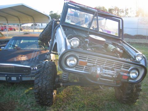 1992 Ford Mustang - A heavily modified SUV with a roll cage and off-road tires sits beside a weathered sedan.