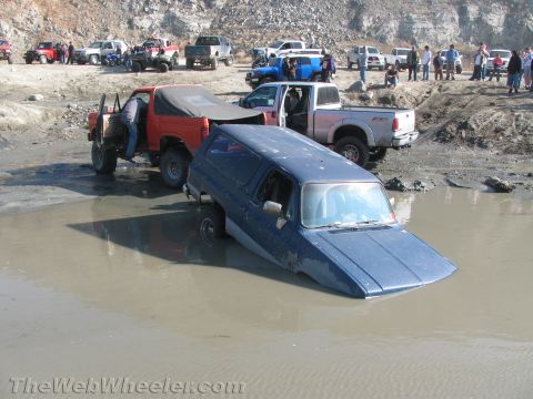 1987 Suzuki Samurai - A blue SUV is stuck in the mud with other vehicles and people in the background.