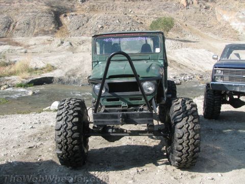 1987 Suzuki Samurai - A heavily modified off-road vehicle with oversized tires and a custom front bumper is parked near a body of water, with another truck visib…
