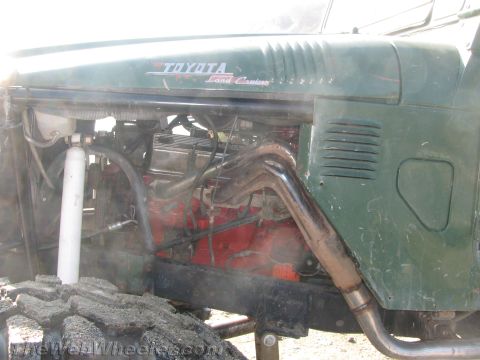 1987 Suzuki Samurai - Close-up of a green Toyota Land Cruiser's engine bay and fender, revealing custom exhaust headers and suspension components.