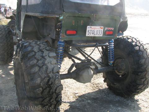 1987 Suzuki Samurai - Rear view of a heavily modified off-road vehicle with oversized tires and custom suspension components.