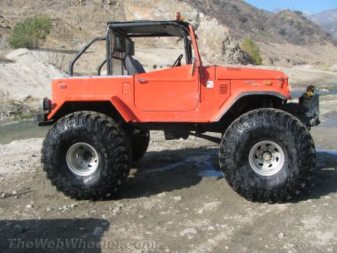 1987 Suzuki Samurai - This modified off-road vehicle features oversized tires and a roll cage, suggesting it is built for terrain.