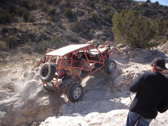 Orange dune buggy climbing rocks, rear-mounted spare tire visible
