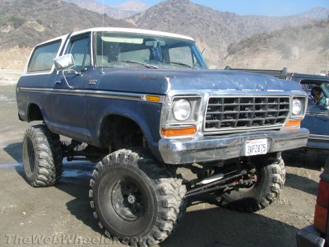 1987 Suzuki Samurai - This lifted Ford Bronco is parked outdoors with mountains in the background and another vehicle to its right.