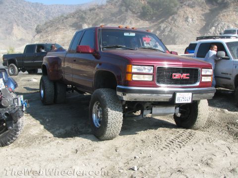 1987 Suzuki Samurai - A maroon GMC pickup truck with dual rear wheels and lifted suspension is parked on a dirt lot with other vehicles.
