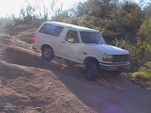 1992 Ford Bronco - A white 1992 Ford Bronco navigates a steep, dusty incline in a natural landscape.