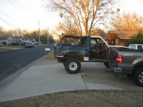 1986 Ford Bronco - A heavily modified Ford Bronco, likely from the early 1980s, is seen attached to a pickup truck bed.