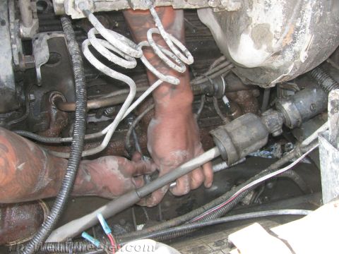 1987 Suzuki Samurai - Close-up of engine bay with mechanic's hands visible, working on various components.
