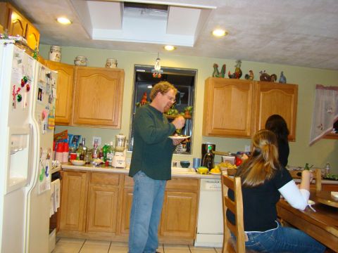 1989 Ford Bronco - A group of people are in a kitchen, with one man standing and eating while others are seated at a table.
