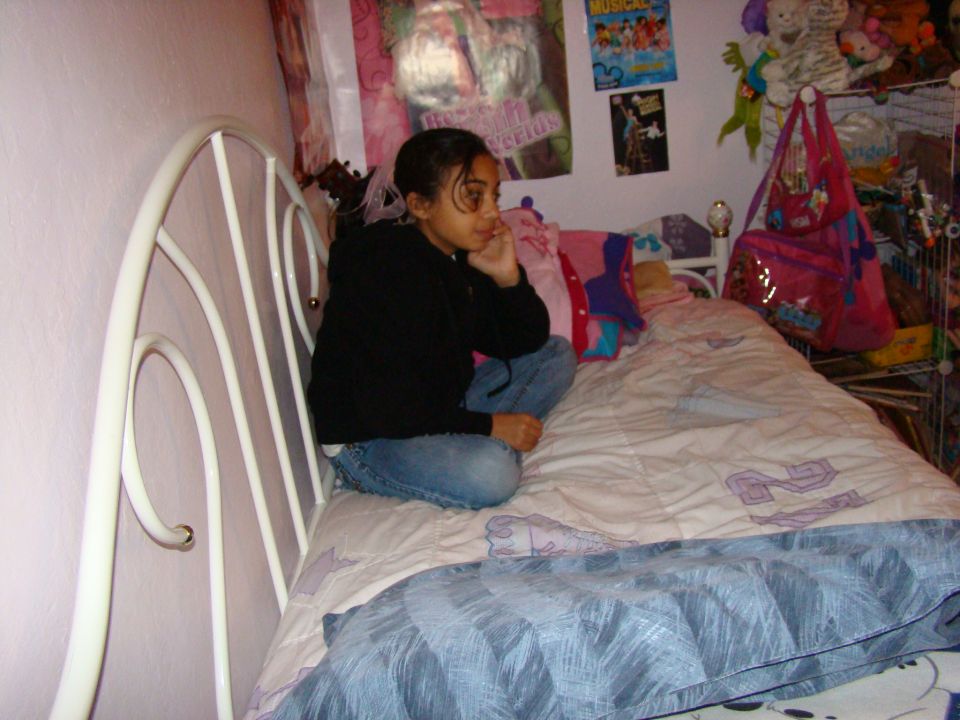 Girl sitting on a bed in a bedroom, looking away