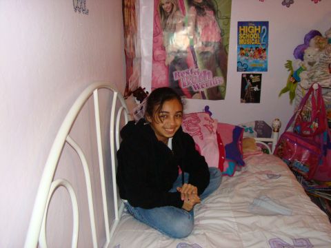 1989 Ford Bronco - A young girl sits cross-legged on a bed in a bedroom decorated with posters and stuffed animals.