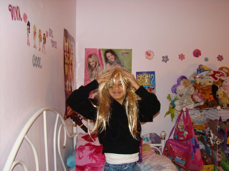 Girl with blonde wig in bedroom with posters and stuffed animals