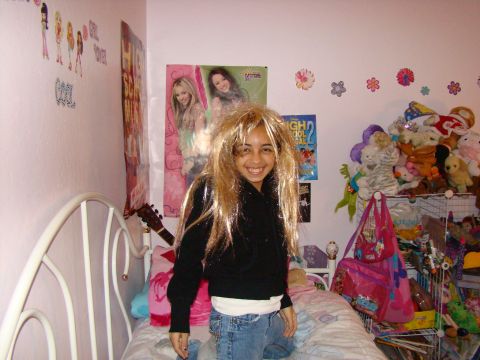 1989 Ford Bronco - A young girl with a blonde wig smiles while kneeling on a bed in a bedroom decorated with posters and stuffed animals.