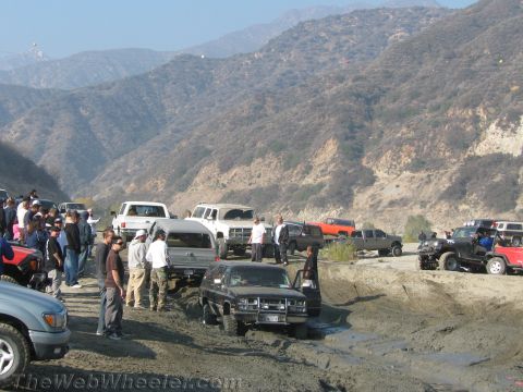 1987 Suzuki Samurai - A group of off-road vehicles navigate a muddy terrain, with onlookers observing the challenging conditions.