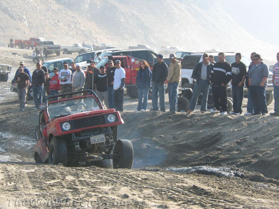 Red Suzuki Samurai off-roading on a sandy hill with a crowd watching