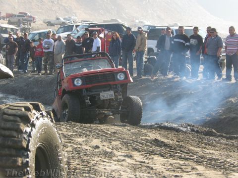 1987 Suzuki Samurai - A red 1987 Suzuki Samurai navigates a muddy off-road course as spectators observe.