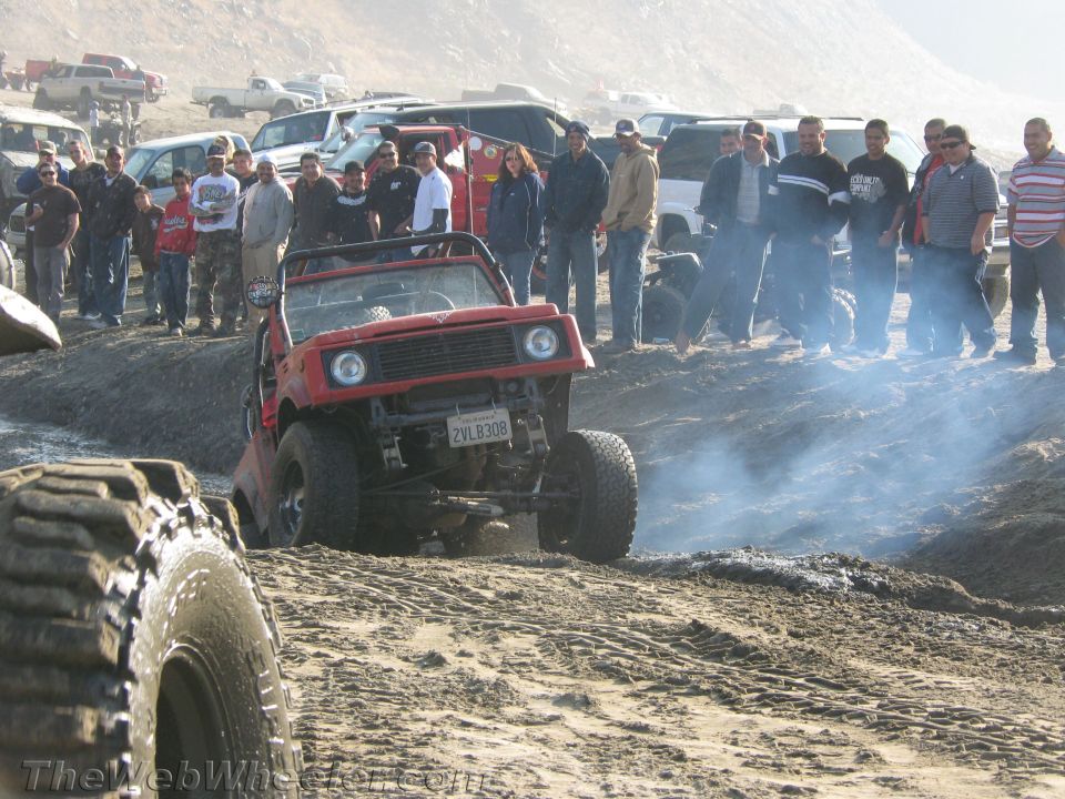 Red 1987 Suzuki Samurai off-roading with a crowd watching