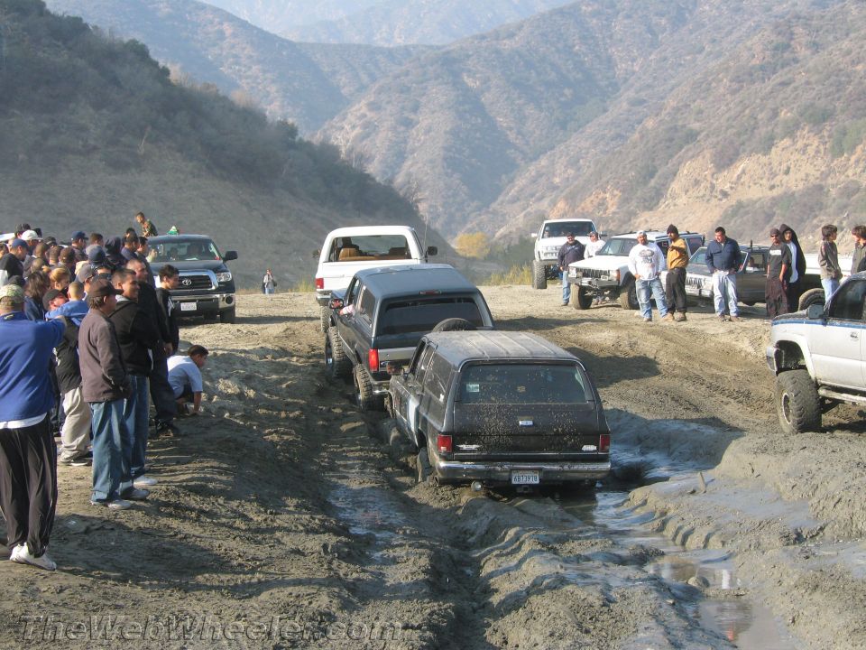 Off-road vehicles navigating a muddy track with spectators watching