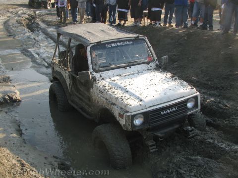 1987 Suzuki Samurai - White Suzuki Samurai navigating a muddy off-road course with spectators watching.