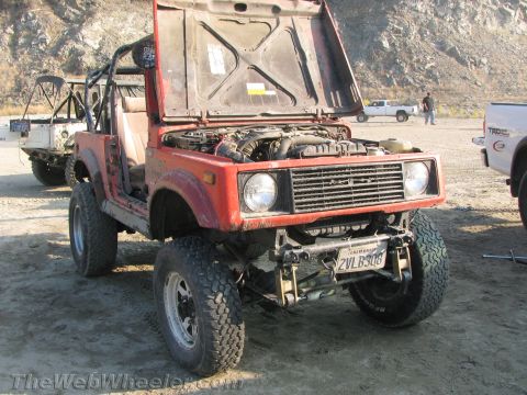 1987 Suzuki Samurai - A red Suzuki Samurai is parked outdoors with its hood open, revealing the engine compartment and off-road modifications.